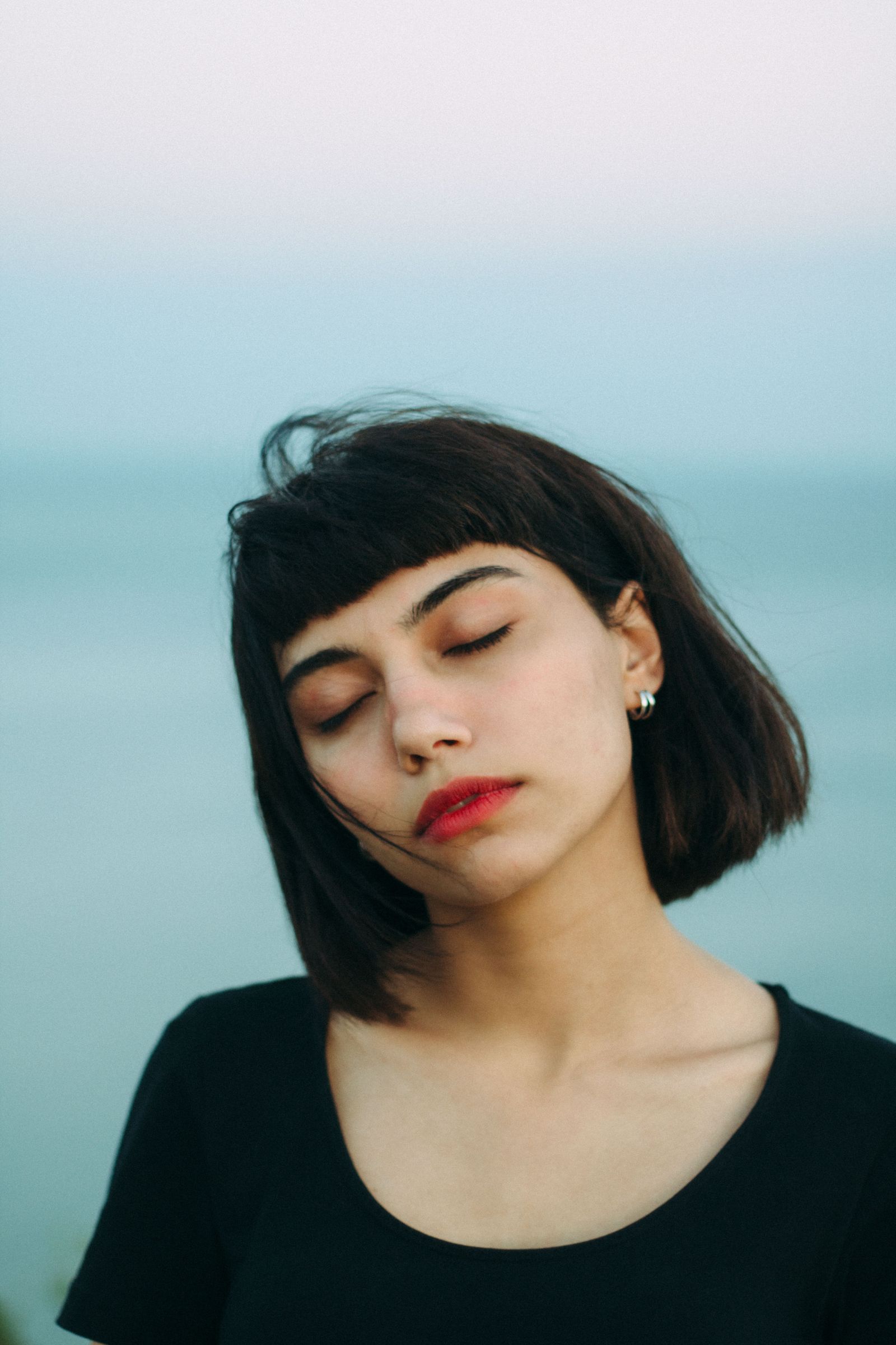 15 Elegant Italian Bob Haircut Ideas for a Sophisticated Look Portrait of a woman with short black bob-length hair and closed eyes near the ocean