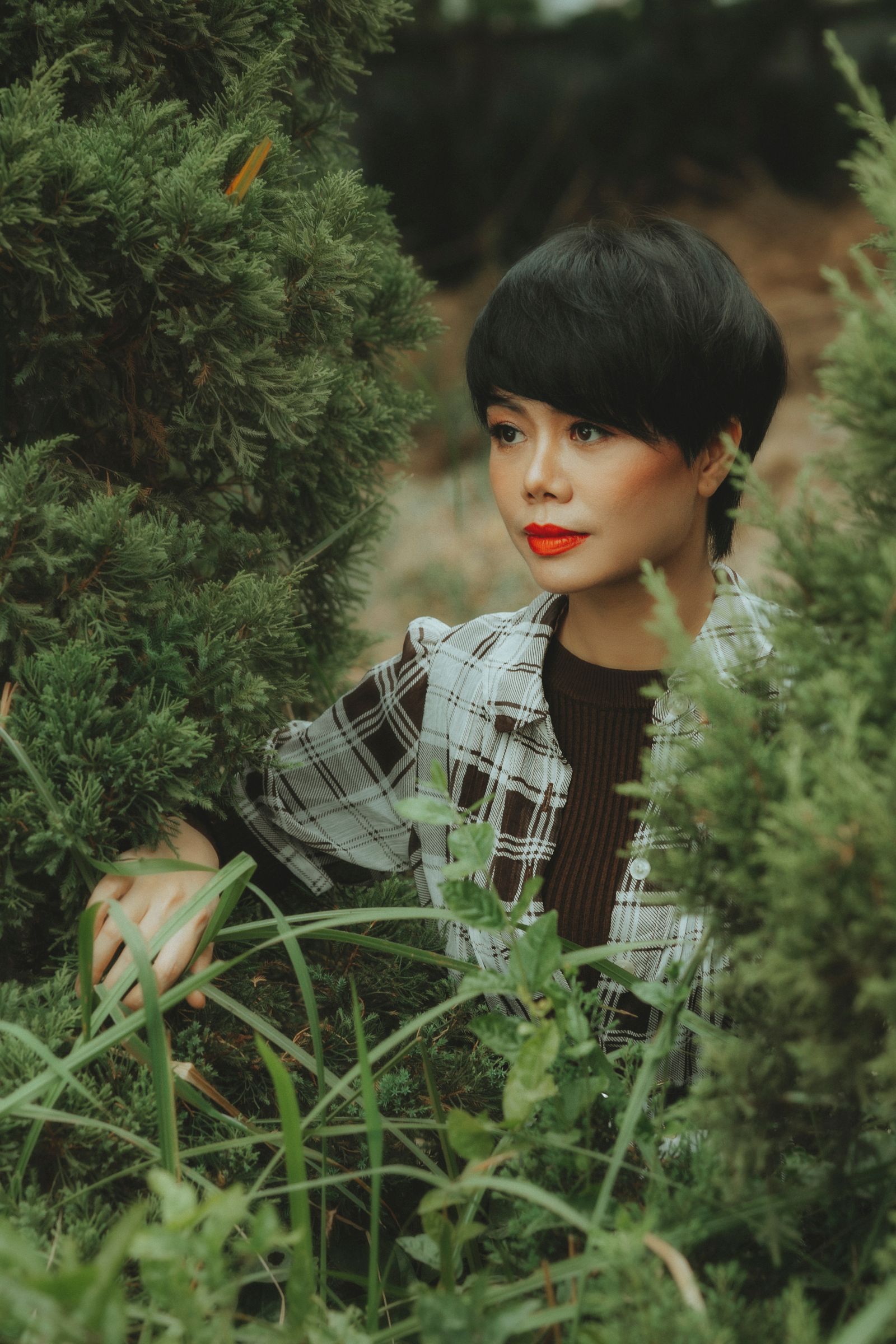15 Trendy Bixie Haircut Ideas You Need to Try in 2026 Portrait of a woman with a short sleek black bixie bob outdoors among green foliage