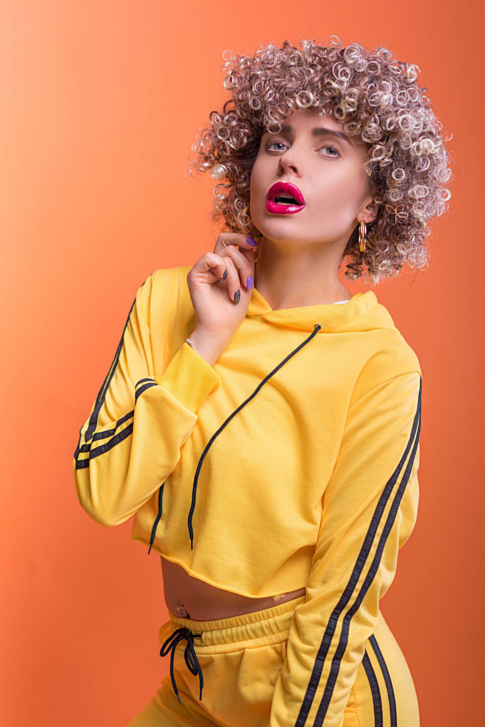 15 Trendy Bixie Haircut Ideas You Need to Try in 2026 Studio portrait of a woman with a short curly bixie haircut, red lipstick and a yellow top
