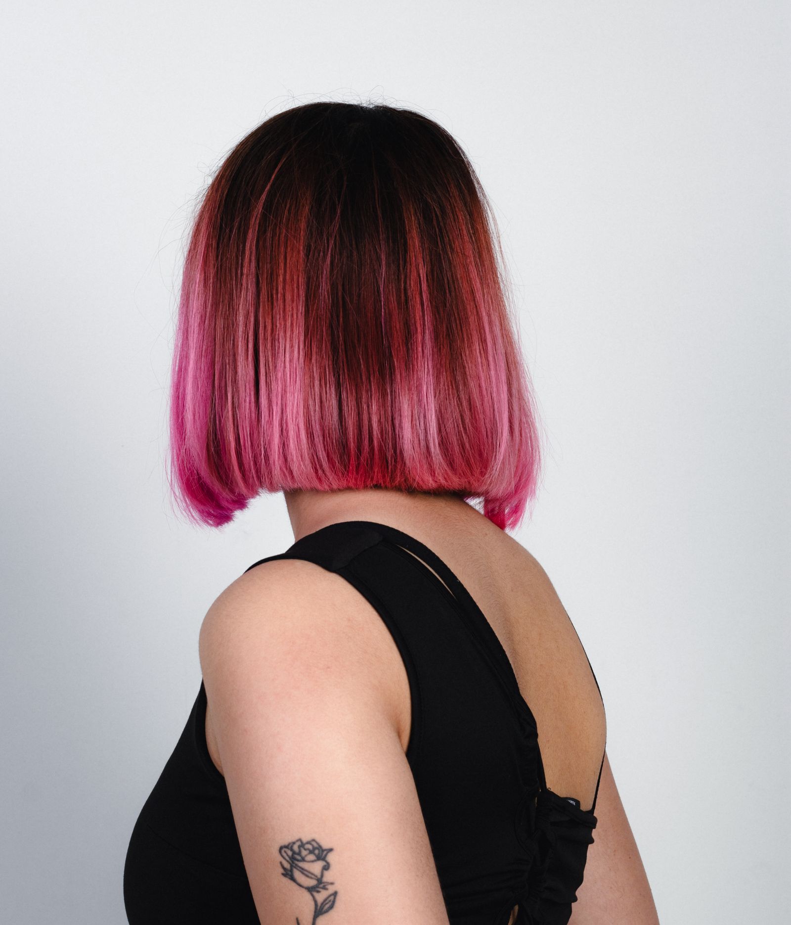 15 Trendy Bixie Haircut Ideas You Need to Try in 2026 Back view of a pink bixie bob haircut in a studio, rose tattoo visible on the arm