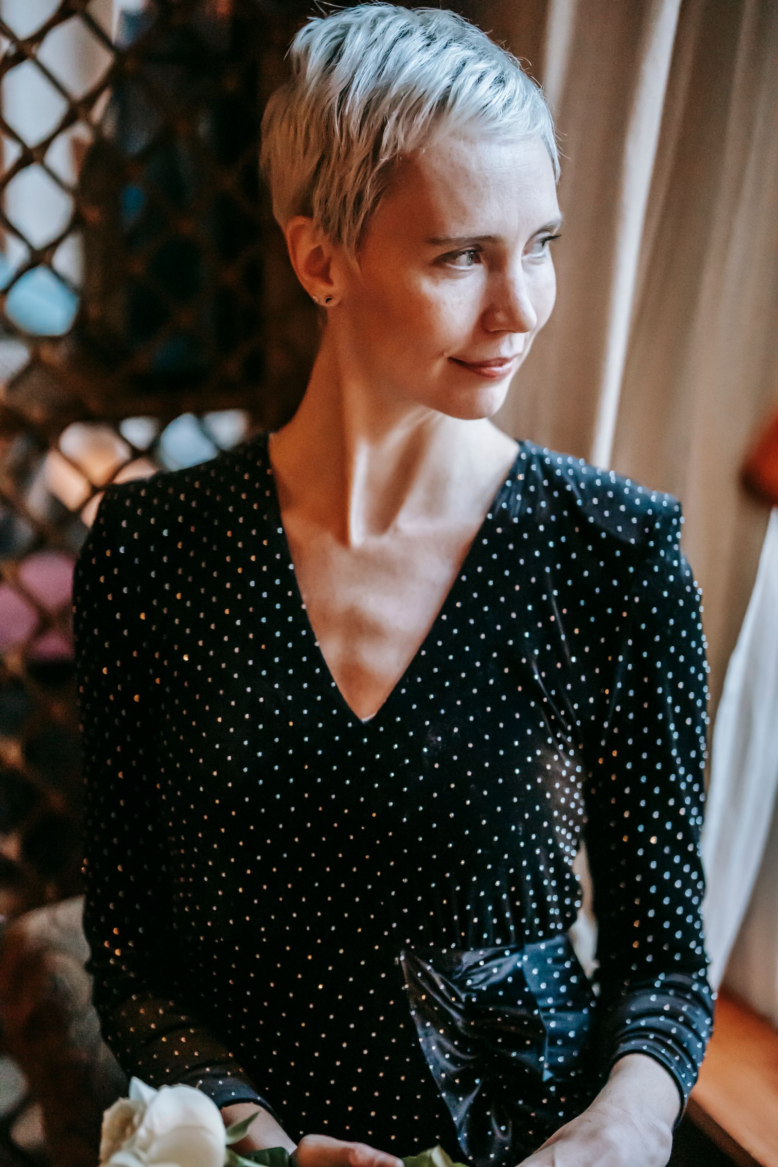 15 Trendy Bixie Haircut Ideas You Need to Try in 2026 Woman with a short blonde bixie bob in an elegant dress, holding a white rose indoors