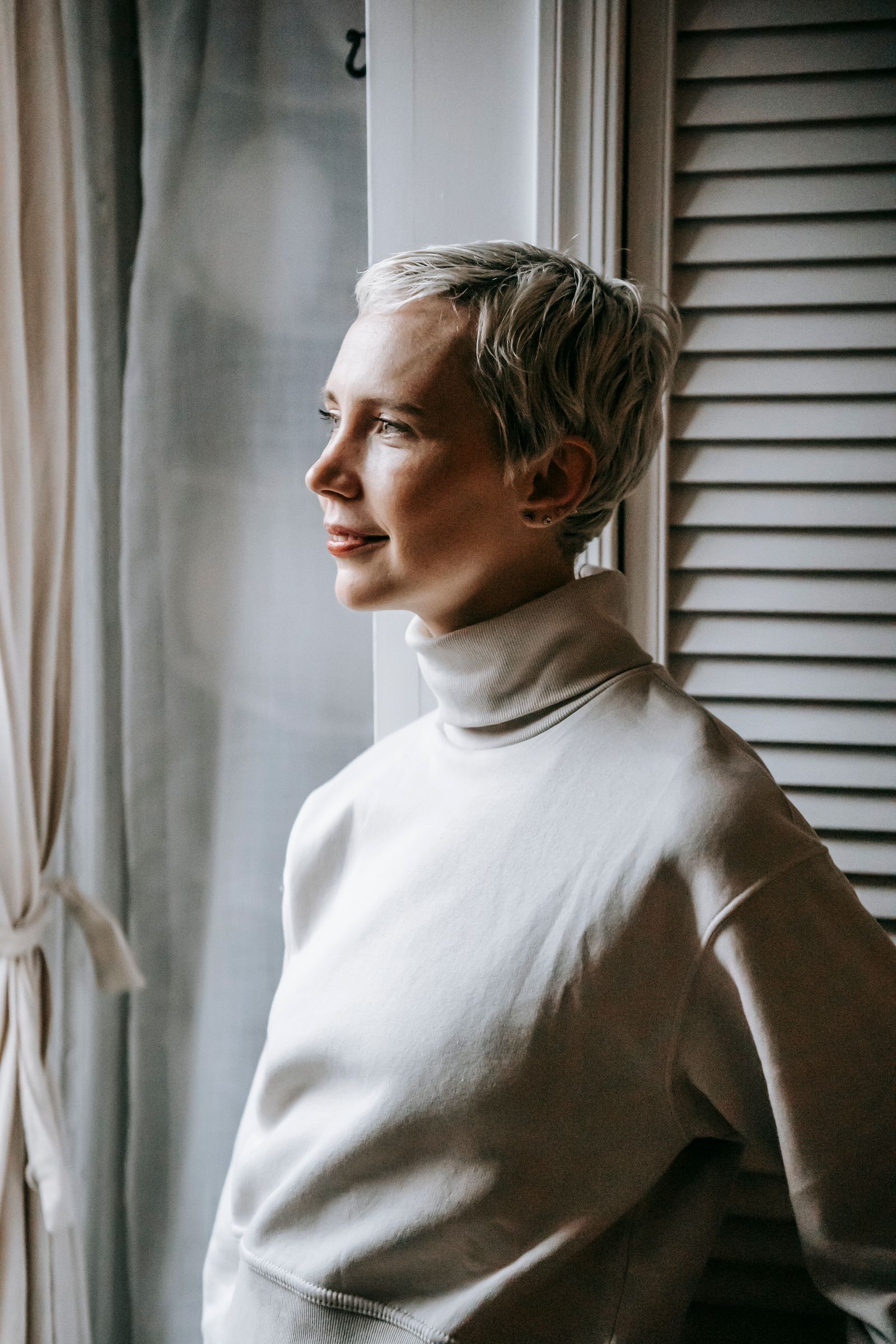 15 Trendy Bixie Haircut Ideas You Need to Try in 2026 Woman with a short dyed bixie haircut standing by a window in soft daylight